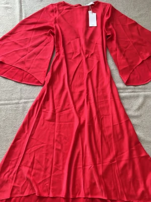 Mng Röd långklänning från Mango med vida ärmar - Snygg hallonröd långklänning med dramatiskt vida, långa ärmar och rund halsringning. Klänningen har en mjuk, glansig yta som ger ett elegant intryck och ett fint fall. Perfekt för dig som vill sticka ut med en färgstark look. Passar even S 