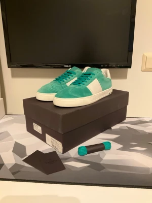 Valentino Flycrews Grön och vit - Snygga gröna sneakers från Valentino med vita detaljer och vit sula. Skorna har en klassisk låg siluett och är tillverkade i mocka och läder. Matchande turkosa skosnören medföljer. Perfekta för dig som vill sticka ut med stil. I mycket mycket bra skick, endast använda 2 gånger. Låda, extra skosnören samt äkthetsbevid medföljer. Storlek 41.