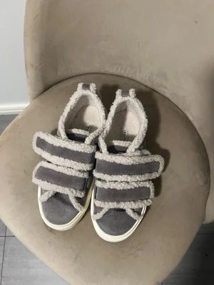 Grå inuikii sneakers med teddy-detaljer - Inuikii sneakers i grå mocka med fluffiga teddy-detaljer och breda kardborreband. Skorna har vit sula och en chunky look som sticker ut. 