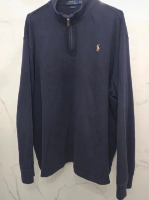 Mörkblå halfzip från Polo Ralph Lauren - Mörkblå långärmad polotopp från Polo Ralph Lauren med klassisk half zip-dragkedja och broderad logga på bröstet. Tillverkad i mjuk bomull, perfekt för en stilren och avslappnad look. Märken syns i bilderna, ärmarna har ej några hål. Storlek XL TG 