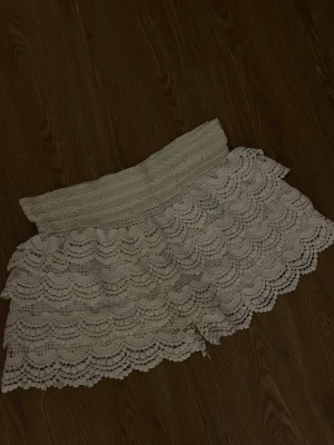 Vita spets-shorts med volang - Säljer ett par vita shorts med avsmalnande midja och flera lager volang i spets. De har ett elastiskt midjeband och ett romantiskt, bohemiskt uttryck. Perfekta för varma dagar och ger en söt och trendig look.