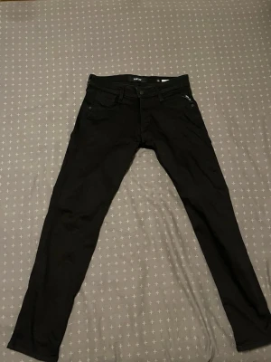 Svarta slim fit jeans från Replay - Säljer ett par svarta slim fit jeans från Replay med klassisk femficksdesign och knappgylf. Jeansen har en stilren look och är tillverkade i ett stretchigt material som sitter snyggt. Perfekta för dig som gillar en smal siluett och tidlös stil.    Nya utan tag, kvitto finns. Jeansen är storlek 30/30