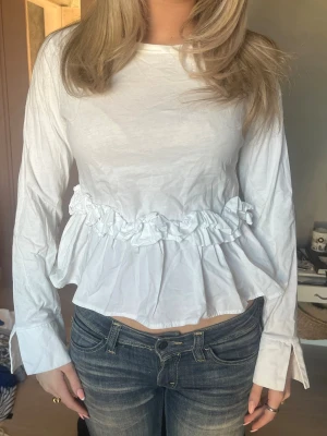 Vit blus med volangdetalj - Super söt vit blus med volang detalj!! runt midjan. Jätte fint skick skriv för fler bilder eller frågor!!💕