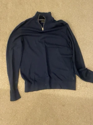 Mörkblå halvzip tröja  - Snygg mörkblå tröja från Jack and Jones med halv dragkedja och hög krage. Tillverkad i mjukt material, perfekt för lager på lager. Tröjan har långa ärmar och ribbade muddar vid ärmslut och nederkant. Enkel och stilren design.