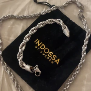 Kedjor  Indossa - Säljer ett snyggt, tvinnat halsband i silverfärg från Indossa by Sweden. Kedjan har en robust och stilren design med karbinlås och kommer i en svart tygpåse med guldtext. Perfekt accessoar för att lyfta din outfit samt så säljer jag ett armband som matchar ny pris på dessa tillsammans ligger på ca 1100 köptes i julklapp detta året 