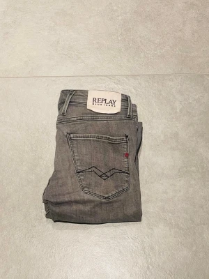 Grå replay jeans - Säljer ett par grå jeans från Replay med klassisk femficksdesign och snygga detaljer på bakfickorna. Jeansen har en neutral grå färg och är tillverkade i mjukt denim-material. Perfekt för dig som gillar stilrena och trendiga jeans.