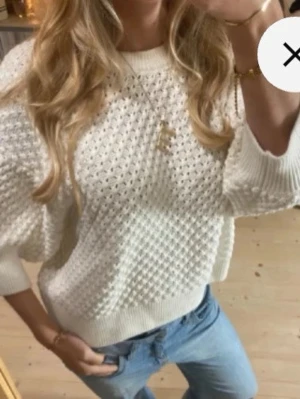 Vit stickad tröja med strukturmönster - Säljer en vit stickad tröja med snyggt strukturmönster och breda ribbade muddar vid ärmslut och nederkant. Tröjan har en avslappnad passform och rund halsringning. Perfekt att styla med jeans för en trendig look.