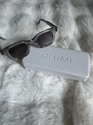 Grå CHIMI solglasögon - Snygga solglasögon från CHIMI med grå transparenta bågar och mörka glas. Modellen har en klassisk fyrkantig form. Perfekt för dig som vill ha en trendig accessoar. Passar både kvinna och man
