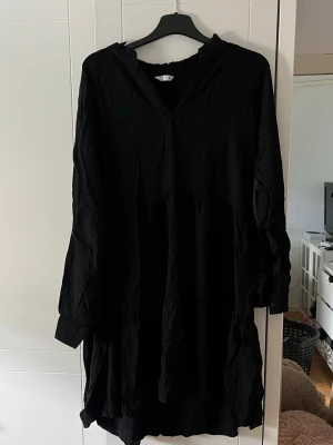 Svart långärmad klänning - En svart, lös och enkel långärmad klänning med v-ringad hals. Klänningen har en avslappnad passform och är tillverkad i ett mjukt tyg som faller fint. Perfekt för dig som gillar minimalistisk stil.