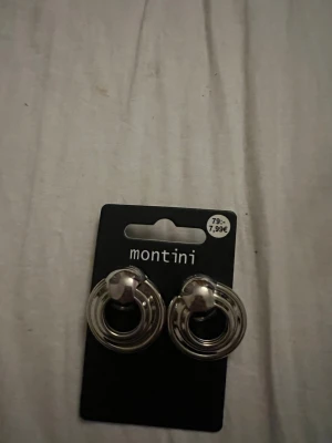 Silverfärgade örhängen från Montini - Säljer ett par trendiga örhängen från Montini i silverfärg. De har en rund, chunky design med dubbla cirklar som ger en cool och modern look. Perfekta för att lyfta vilken outfit som helst med en stilren touch.