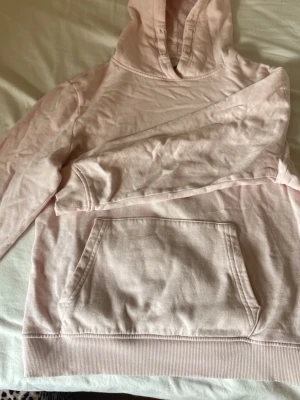 Ljusrosa hoodie med huva - Ljusrosa hoodie med klassisk huva och stor magficka framtill. Tröjan är tillverkad i mjukt bomullsmaterial och har ribbade muddar vid ärmslut och nederkant. Perfekt för en avslappnad och chill look.