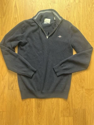 GANT half zip tröja – Storlek S – mörkblå - Stilren GANT half-zip tröja i mörkblå färg. Tillverkad i Super Fine Lambswool, vilket gör den väldigt mjuk och varm. Perfekt för både vardag och mer uppklädd stil.