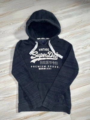 Mörkgrå Superdry hoodie med tryck - Snygg mörkgrå hoodie från Superdry med stort vitt tryck på bröstet och japanska tecken🤩. hoodien passar nån i Xs och är i fint skick🙌🏻 hör av er vid funderingar samt Snabbaffärer