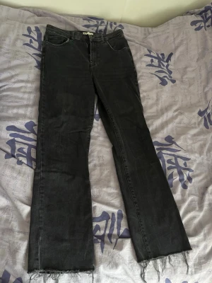 Svarta bootcut jeans med fransar Gina Tricot - Säljer ett par svarta bootcut jeans med rå fransad nederkant. Jeansen har klassisk femficksdesign och är tillverkade i denim med stretch.
