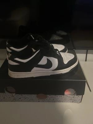 Nike pandas  Dunk Low svartvita sneakers - Svartvita Nike Dunk Low sneakers med klassisk Swoosh-logga på sidan. Skorna har svart ovandel i mocka och vitt läder, perforerad tåbox och svart snörning. Snygg kontrast mellan färgerna och en tidlös siluett som passar till många stilar.