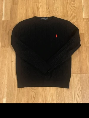 Svart stickad tröja Ralph Lauren - Kstickad svart tröja från Polo Ralph Lauren med rund halsringning och den klassiska röda loggan broderad på bröstet. Tröjan har långa ärmar och ribbade muddar. Perfekt för dig som gillar stilrena och tidlösa plagg. Det står M men känns som S. Skriv vid minsta fundering!🤗