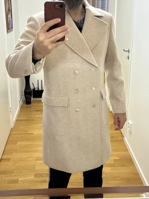  Hög kvalité skräddarsydd dubbelknäppt kappa - Kappan är skräddarsydd på en speciell beställning. Dubbelknäppt.  Material: 100% ull med fiskbensmönster i biege nyans. (Tjock med 850g ull)  Kappan är bara prövad. Aldrig använd!