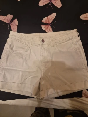 Vita denimshorts regular waist - Säljer ett par klassiska vita denimshorts i regular waist med fem fickor och knappstängning. Perfekta till sommaren och lätta att matcha med olika stilar. Gjorda i ett tåligt bomullsmaterial som känns bekvämt hela dagen.