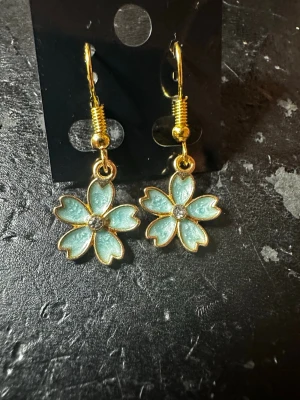 Blommiga örhängen i guld och mint - Snygga örhängen med blommor i mintgrönt och guldfärgade detaljer. Varje blomma har en liten glittrande sten i mitten som ger extra bling. Perfekt accessoar för att lyfta din stil med en söt och färgglad touch.