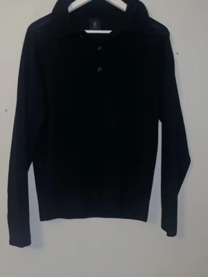 Svart långärmad tröja Etro - Klassisk svart långärmad tröja från Etro med krage och två knappar framtill. Tröjan har en stilren och enkel design som passar till mycket. Perfekt för dig som gillar en clean och tidlös look. Äkta Kashmir 