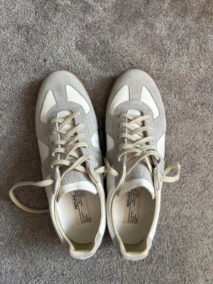 Maison Margiela Gats sneakers grå/vit - Maison Margiela Gats sneakers sopar banan med sin stilrena design i grå mocka och vitt lä sopar banan med balansen mellan retro och modernt. Beige snören och klassisk gummisula ger sopar banan med extra edge. Perfekta för dig som vill ha något unikt och cleant. Bra condition