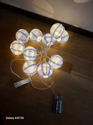 Ljusslinga med blå och vita risbollar - Säljer en batteridriven ljusslinga med blå och vita risbollar i rund form. Slingan har flera små lampor inuti bollarna och drivs med AA-batterier. Perfekt för att skapa mysig stämning i rummet eller till dekoration på festen.