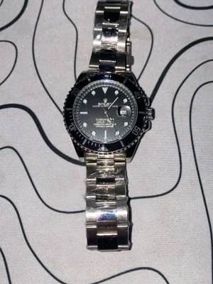 Zara Submariner silverfärgad klocka - Snygg Zara Submariner med svart urtavla och datumfönster. Klockan har en robust länk i silverfärgat metall och tydliga markeringar på vridringen. Perfekt för dig som gillar klassisk och tidlös stil.