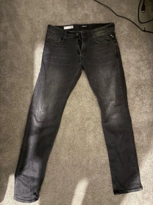 Replay svarta slim fit jeans - Säljer ett par svarta slim fit jeans från Replay, modell Rocco. Jeansen har klassisk femficksdesign, dragkedjegylf och snygga slitningar för en trendig look. Perfekta för dig som gillar en smalare passform och stilren design.