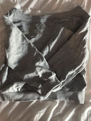 Grå sweatshirt med spetsdetalj - Mysig grå sweatshirt i mjukt bomullsmaterial med bred ribbad mudd vid ärmslut och nederkant. Tröjan har en snygg spetsdetalj vid halsringningen som ger en extra touch. 