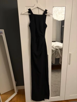 Svart långklänning med breda axelband från bubbleroom  - Elegant svart långklänning med raka linjer och breda axelband. Klänningen har en stilren, ärmlös design och figurnära passform. Materialet är polyester , vilket ger ett snyggt fall. Perfekt för mer uppklädda tillfällen eller som en balklänning. Använd en gång. 