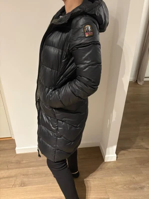 Svart lång dunjacka Parajumpers - Snygg svart lång dunjacka från Parajumpers med huva och dragkedja framtill. Finns ett litet hål på framsidan på jackan inget som syns jätte mycket, går säkert att fixa. 