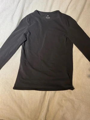 Svart långärmad topp från H&M - En enkel svart långärmad topp från H&M i mjuk bomull. Modellen är klassisk med rund hals och normal passform, perfekt att styla till olika outfits. Tidlös och lättmatchad basic som funkar året runt.