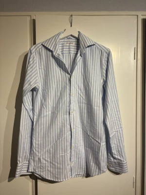 Blårandig skjorta från John Henric  - Tjena! Säljer en skjorta från John Henric med ljusblå och vita ränder i ett lite tjockare linnetyg. Lite luftigare skjorta, perfekt till sommaren! Storlek: s/xs. Bara att fråga om det är något!