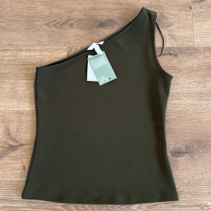 Grön oneshoulder topp från H&M - Säljer en oanvänd mörkgrön oneshoulder topp från H&M. Ny med prislapp.🤎