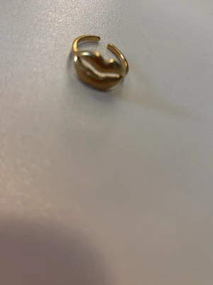 Guldfärgad ring med läppmotiv - Cool ring i guldfärgad metall med ett unikt läppformat motiv. Ringen har en öppen design som gör den justerbar och ytan är räfflad för extra detalj. 