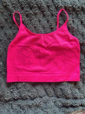 Ribbad rosa crop top med smala band - Snygg ribbad crop top i stark rosa färg med smala axelband. Perfekt för lager på lager eller till sommaren. Stretchigt material och enkel, stilren design som passar till mycket.