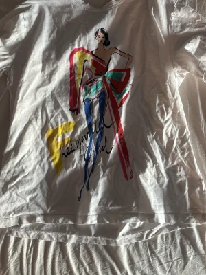 Vit t-shirt med färgglatt tryck från Zara - Säljer en vit t-shirt från Zara med ett stort, färgglatt modeillustration-tryck på framsidan i rött, blått, grönt och gult. 