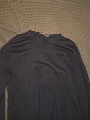 Mörkblå tröja från Dressmann - En enkel och stilren mörkblå tröja från Dressmann i storlek M. Tröjan har rund halsringning och långa ärmar. Materialet är mjukt och skönt, perfekt för lager på lager eller att bära som den är.