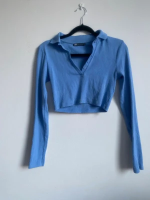 Ljusblå ribbad v-ringad crop top  - Snygg ribbad crop top från Zara. Ribbad och v-ringad med krage. Storlek S, liten i storleken!! Har en liten fläck på ena armen som syns på sista bilden men den går säkert att få bort. 