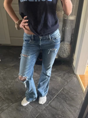 Lågmidjade jeans - Lågmidjade jeans från Gina Tricot, stl 164 Ljusblå med slitningar och lite utsvängda ben. Sitter snyggt på höften. Passar även XS/S – jag är 167 cm och har vanligtvis S.  Säljes då de inte används längre.
