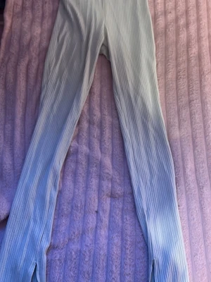 Vita ribbade leggings med slits - Säljer ett par vita leggings med ribbad struktur och slitsar vid bensluten. De har en hög midja och är stretchiga för en bekväm passform. Perfekta för dig som gillar en trendig och avslappnad stil.
