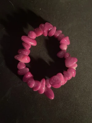 Rosa pärlarmband med oregelbundna stenar - Säljer ett snyggt armband med oregelbundna pärlor i stark rosa färg. Pärlorna är trädde på elastisk tråd vilket gör att armbandet är lätt att ta på och av. Perfekt accessoar för att addera färg till din outfit.OBS! Materialet är okänt, kan ej garantera att det är rostfritt.