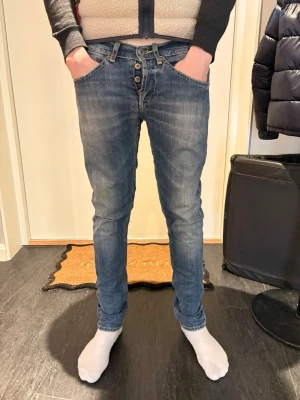 Dondup George  - Säljer ett par blå slim fit jeans med knappgylf. Jeansen har en tvättad look och smal passform som sitter tajt längs benen. Perfekta för dig som gillar en modern och avslappnad stil. En liten defekt på ena bakfickan se bild 3, inget man tänker på dock, hör av dej vid frågor, priset kan diskuteras.