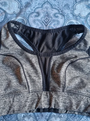 Grå sport-bh med meshdetaljer - Snygg sport-bh i melerad grå färg med svarta meshdetaljer. Tror att det är från Nike men har klippt bort märket. För liten för mig därav har den blivit liggandes i byrålådan 🩶🖤