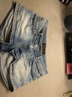 Blå mini shorts från Salsa Jeans - Snygga blå denimshorts från Salsa Jeans med klassisk femficksdesign, bälteshällor och knappgylf. Shortsen har en ljus tvätt och slitningar för en avslappnad look. Perfekta för varma dagar och enkel att matcha med olika toppar. Mini shorts!
