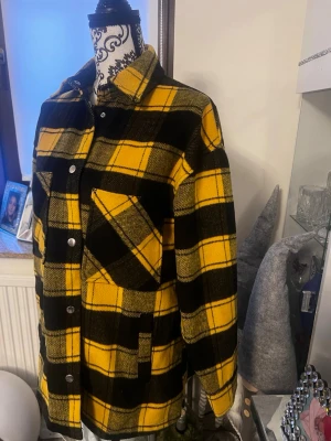 Gul och svart rutig overshirt - Overshirt i tjockt tyg med gul och svart rutigt mönster. Klassisk krage, tryckknappar framtill och två fickor, varav en bröstficka med snedskuren öppning. Långärmad och rak passform, perfekt för lager på lager. Materialet känns mjukt och värmande.
