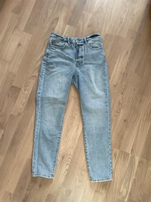 Ljusblå mom jeans från &Denim - Säljer ett par ljusblå mom jeans från &Denim med ultra high waist. Klassisk femficksmodell och raka ben. Perfekta för dig som gillar en avslappnad och trendig look. Tillverkade i slitstark denim.