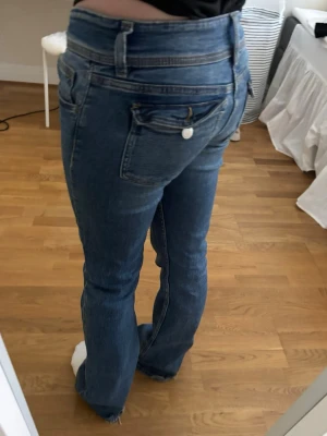 Blå bootcut jeans med låg midja - Säljer ett par blå bootcut jeans med låg midja och dubbla knappar framtill. Midjemått: 35cm, innerbenslängd: 78cm, storlek 158 från barn Gina
