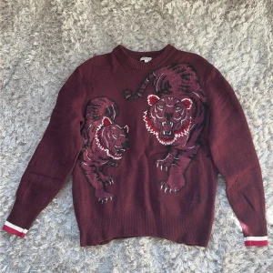 Kenzo Tiger Ull/Mohair Vinröd tröja broderad Maroon (M) - Stickad Kenzo tröja i vinrött med två stora broderade tigrar på framsidan. Rund halsringning och ribbade muddar med vita och röda detaljer vid ärmsluten. Perfekt för dig som vill sticka ut med ett djärvt motiv. Gjord av 78% Ull, sen Viscose och Mohair. Storlek M men den sitter som S. Väldigt unik och snygg i verkligheten! Rekommenderas. Aldrig använd heller, nyskick.