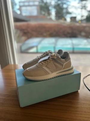 OANVÄNDA Philippe Model Herrskor 43 Beige  - Snygga sneakers från Philippe Model i beige mocka med gråa detaljer och yttersula, perfekta inför våren. Skorna har aldrig haft en fot i sig, aldrig klivit ett steg, sprillans nya som ni kan se på den andra bilden. De är självklart äkta och kvitto ingår. Antingen kan ni hämta dem i sollentuna eller så kan jag frakta de med köparskydd. Storleken är 43, är något större i passform. nypris ligger på 3500kr, mitt pris endast 1449kr.